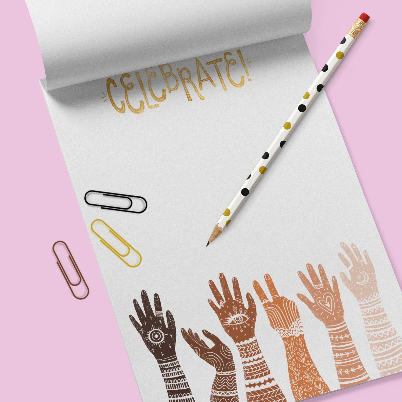 White note pad with diverse multi racially colored hands with arms extended up. the word Celebrate is at the top. Notepad sits on a lavender colored background.