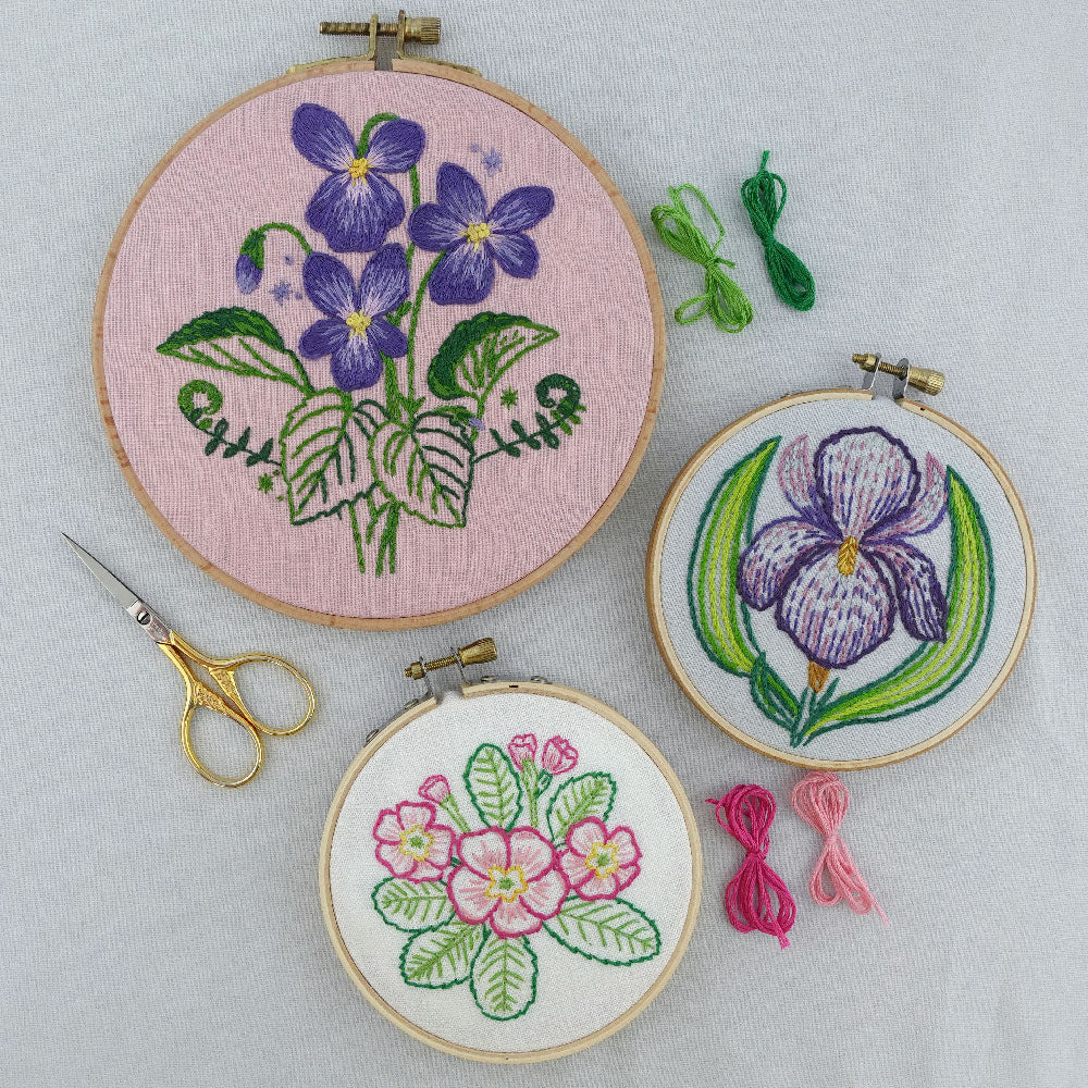 Embroidery hoops with hadn embroidered floral designs from the February chapter of Birth Flower Embroidery on a light gray background