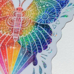 Video of a Butterfly shaped rainbow glitter sticker with white outline on a  white background.