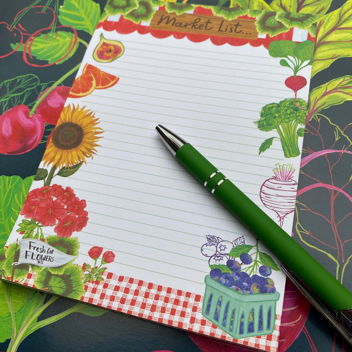 black background with colorful fruits and vegetables. A Market List Notepad sits on top of this illustration containing illustrations of fruits, vegetables and flowers.  A green pen sits on top of the notebad. 