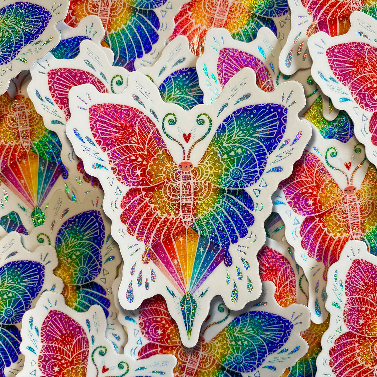 Butterfly shaped rainbow glitter sticker with white outline on a backgound of glitter rainbow stickers