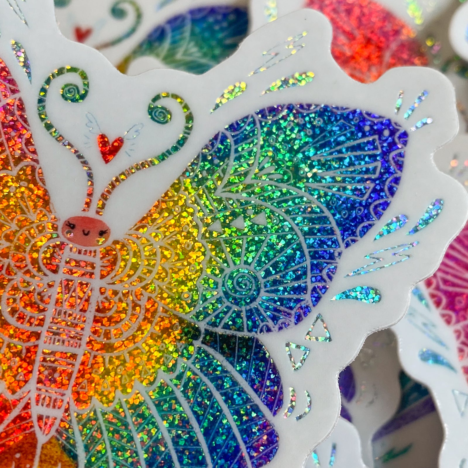 Butterfly shaped rainbow glitter sticker with white outline on a mint green background.