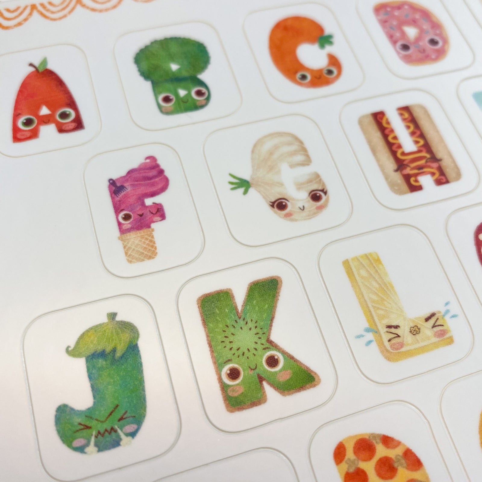 White sheet full of colorful stickers. Each letter represents a fun food character. A, Apple, B Broccoli, C carrot, D Donut , E egg and so on. 